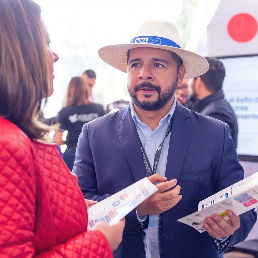 Ejecutiva conversando con expositor con sombrero en venue de CIMEDU®